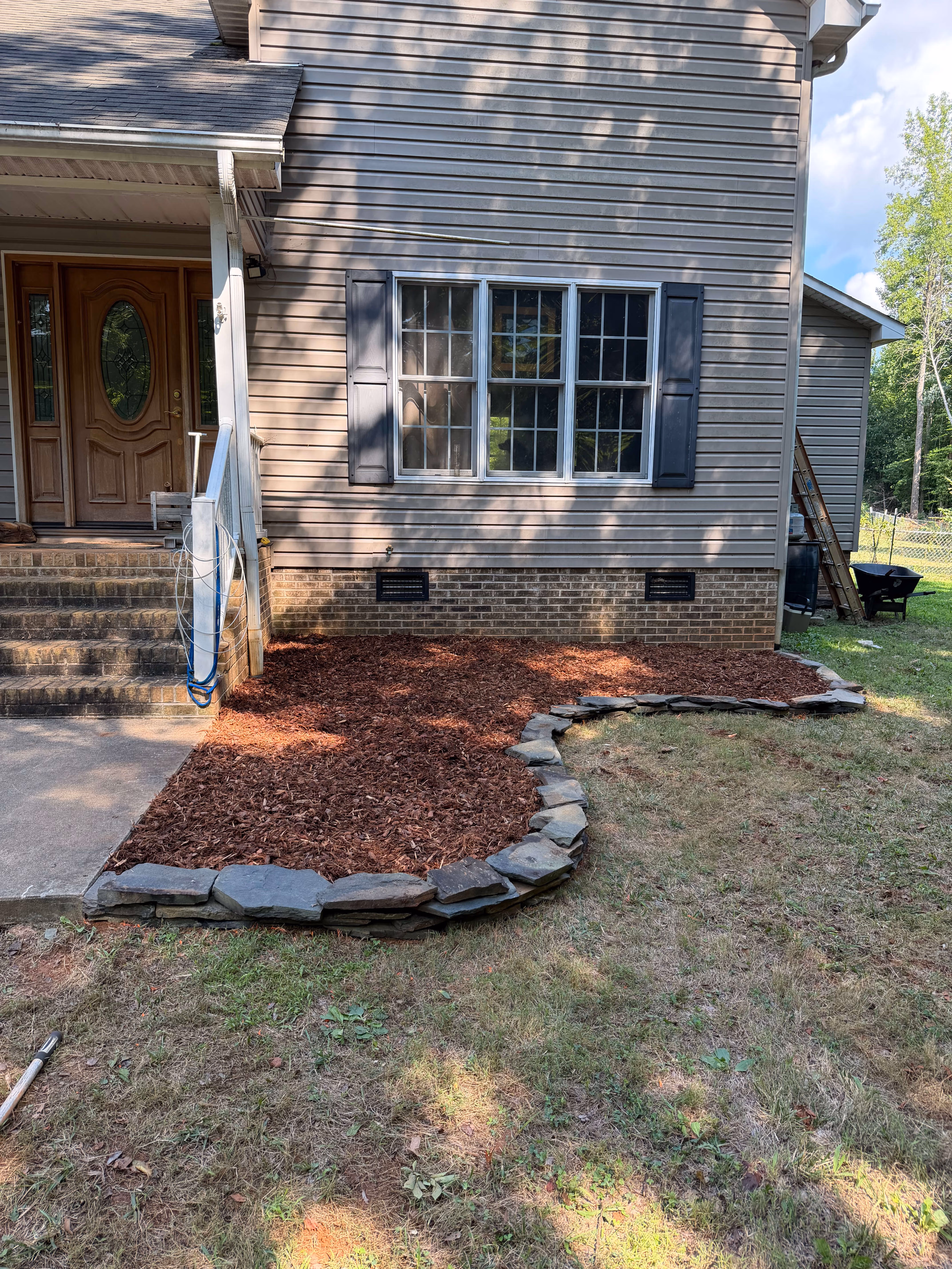 Stone pathway with mulch edging leading to porch stairs of a brick house with a Mickey Mouse birdbath and a CPI security sign in the grass.