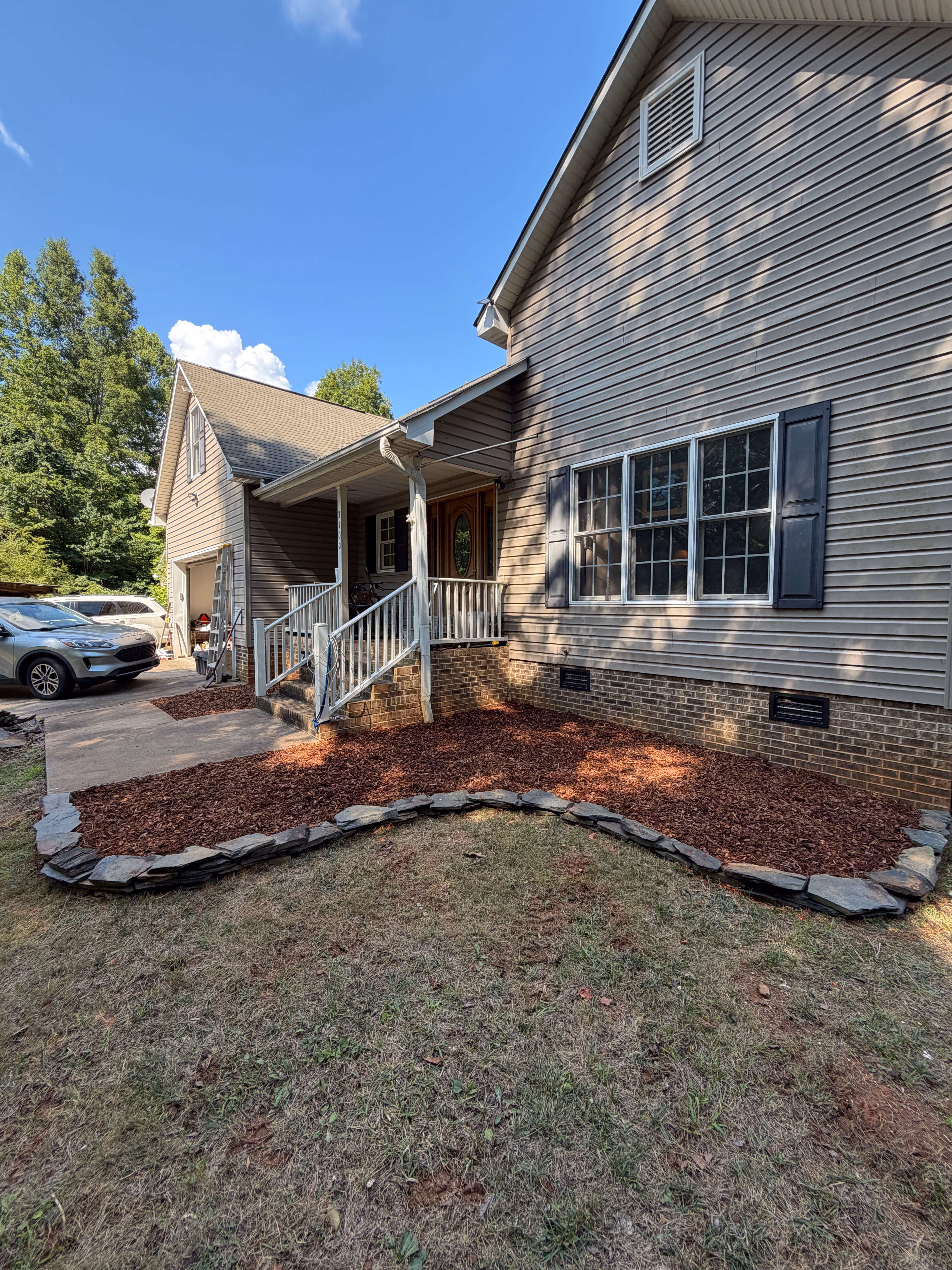 Stone pathway with mulch edging leading to porch stairs of a brick house with a Mickey Mouse birdbath and a CPI security sign in the grass.