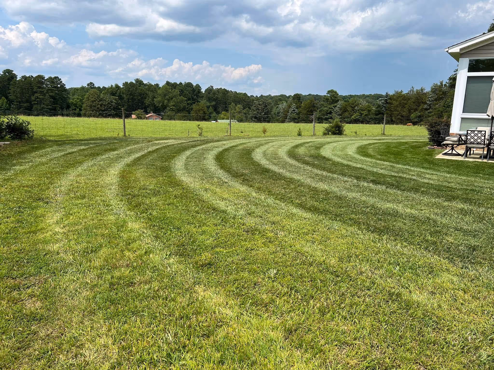 Curved mowing lines on a well-maintained green lawn next to a house patio with outdoor furniture.